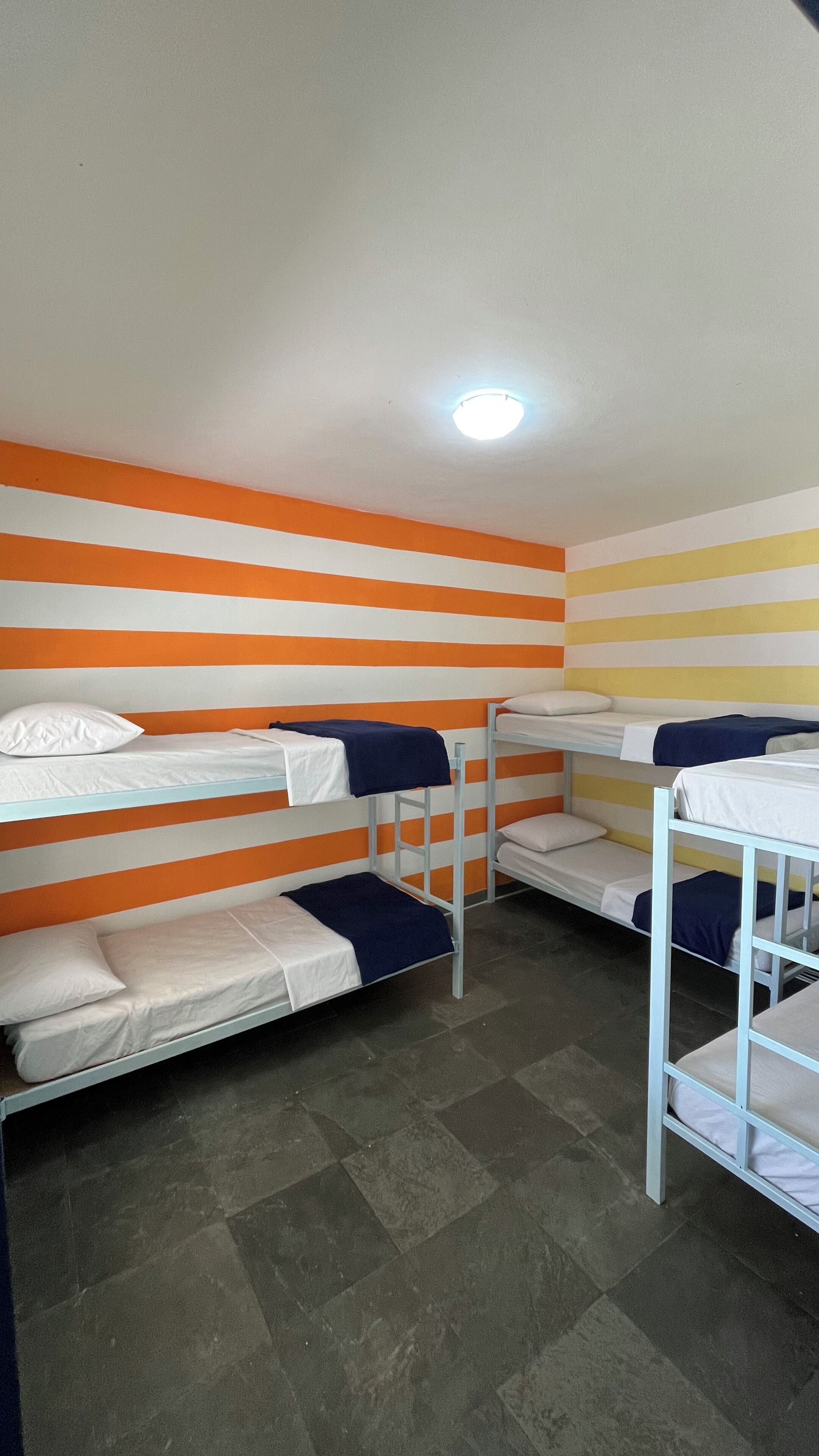 A dormitory room with bunk beds, a tiled floor, and a ceiling light.
