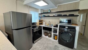 Una cocina funcional con refrigerador de acero inoxidable, horno empotrado, microondas y lavadora.