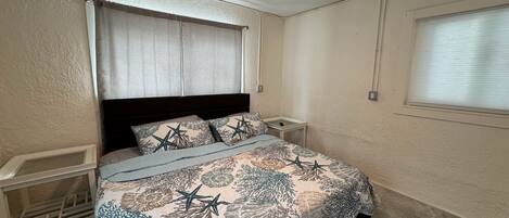 A bedroom with a bed, nightstands, a ceiling fan, and a window with blinds.