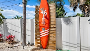 Una tabla de surf montada en una pared de madera, rodeada por una cerca blanca y palmeras.