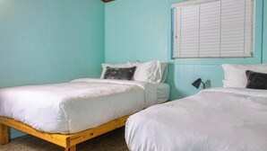 A room with two wooden beds, white bedding, and a window with blinds.