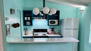 A kitchen with teal walls, a white countertop, a black stove, a white refrigerator, and two black bar stools.
