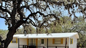 A single-story building with a white exterior and yellow trim. It features a front porch with a wooden railing and a small staircase leading up to the entrance.