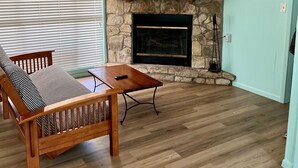 A living room with a stone fireplace, a flat-screen TV mounted above it, a wooden sofa, and a coffee table.