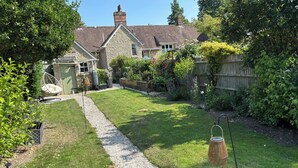 A well-maintained garden with a gravel path leading to a house with stone walls and a tiled roof.