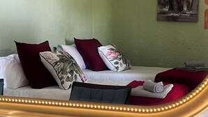 Habitación de hotel con cama, almohadas, una colcha roja y cabecera con luces.