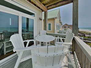 A deck with white chairs and a table, overlooking a beach and a house with a green roof. - Sea For Miles by Topsail Realty (Sneads Ferry)