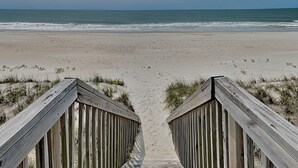 A wooden boardwalk leading to a beach with sand dunes and ocean views.