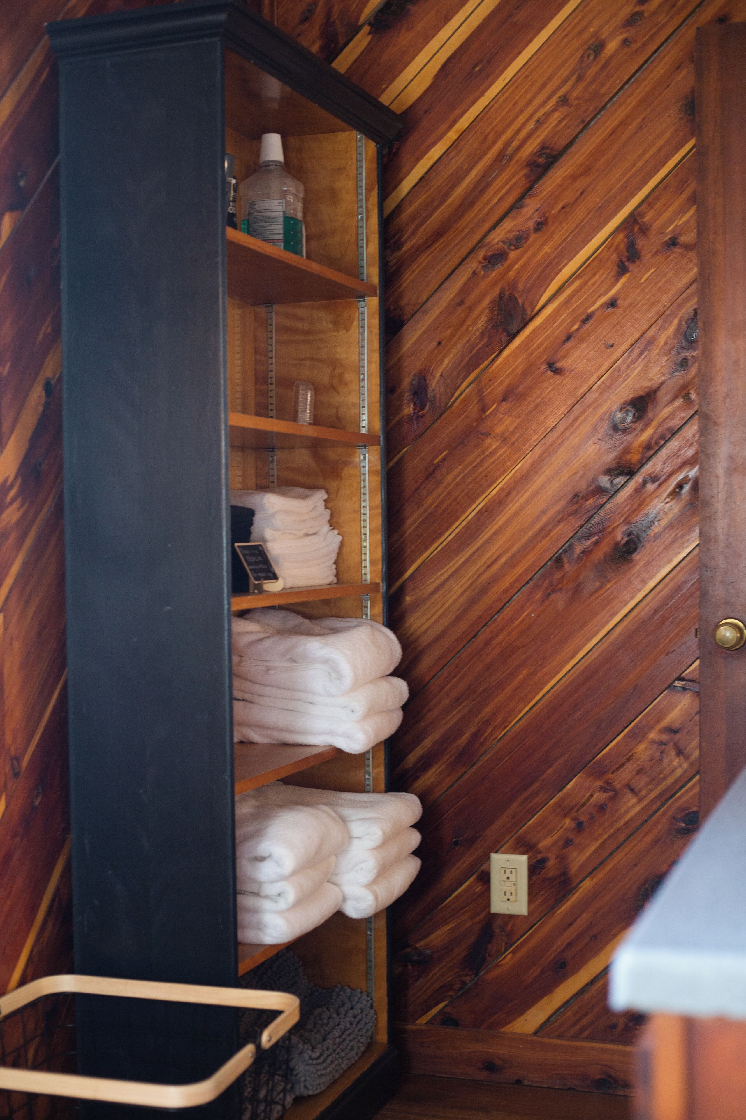 A wooden wardrobe with shelves holding folded towels and a bottle of lotion.