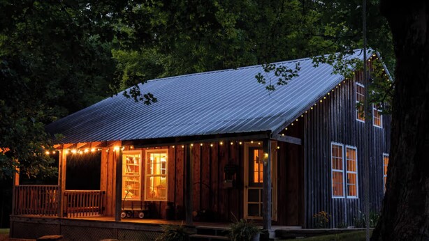 A rustic cabin with a porch, wooden exterior, and string lights.