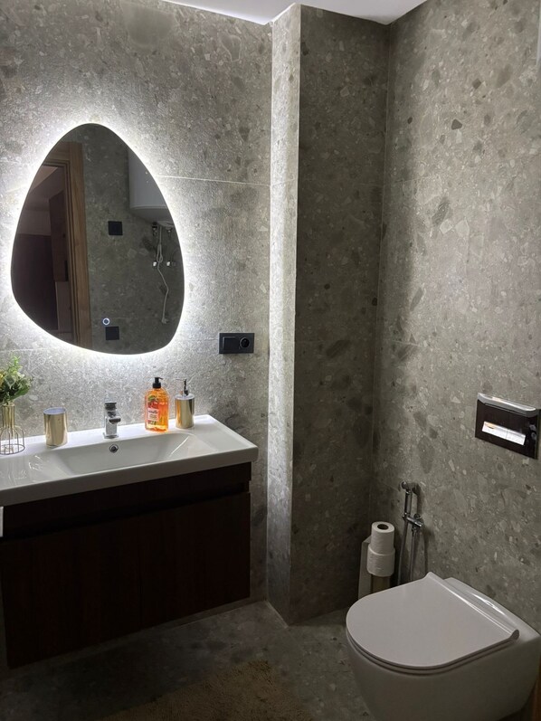 Un baño con un espejo grande, un lavabo con artículos de aseo, un inodoro y una ducha.