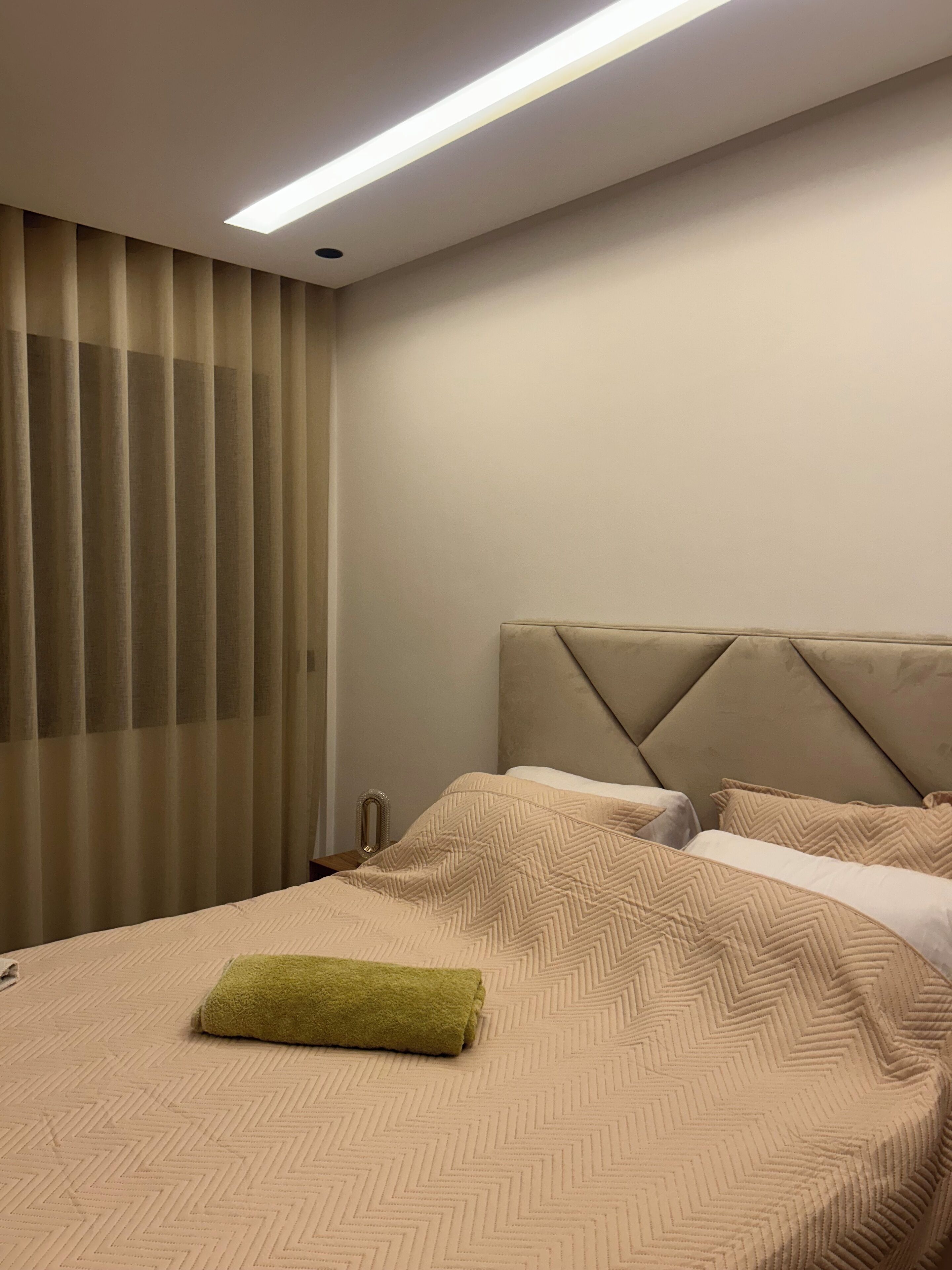 A hotel room with a bed, a headboard, and a window with curtains.