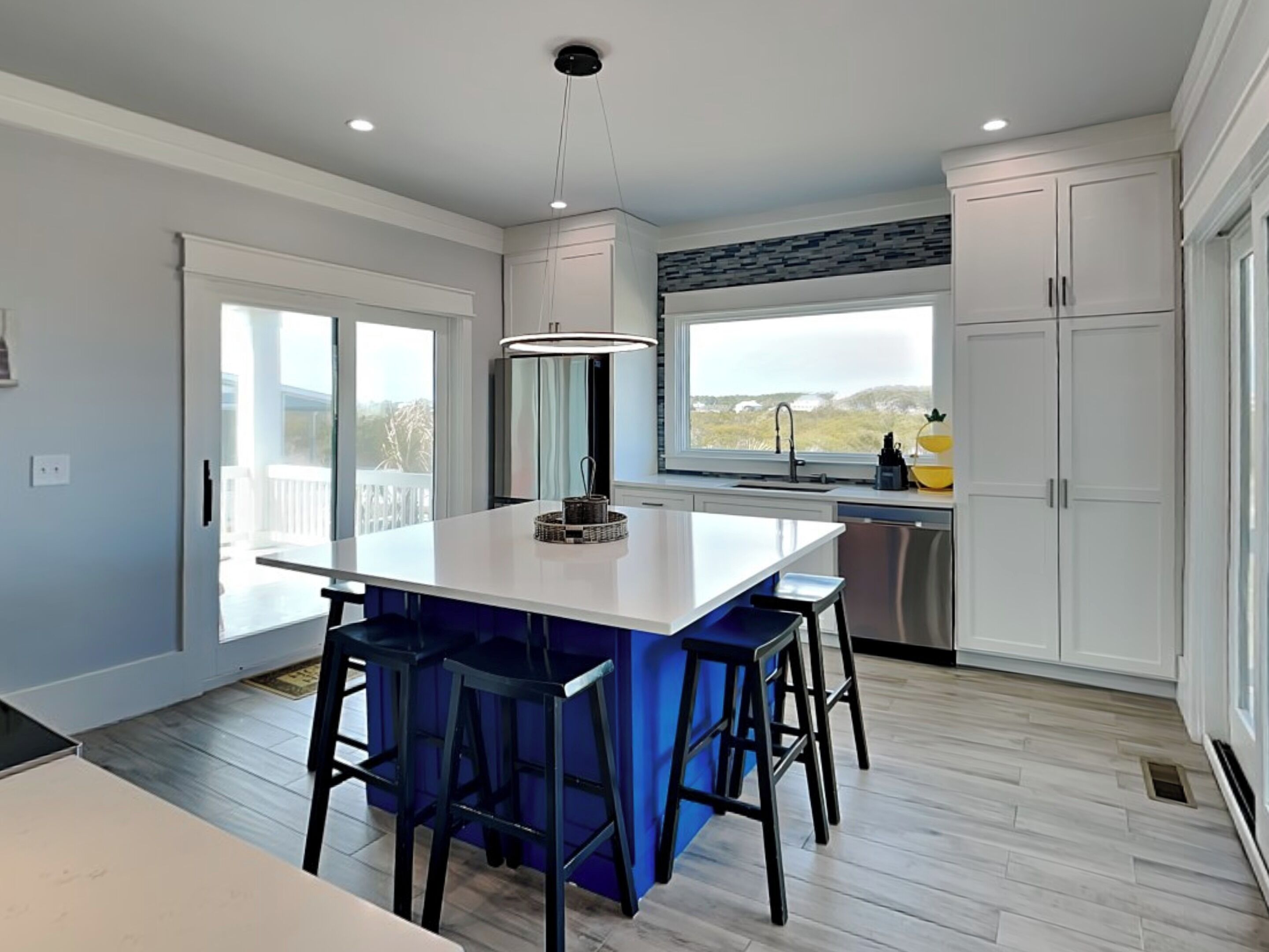 A modern kitchen with a central island, bar stools, a large window, and a view of the outdoors.