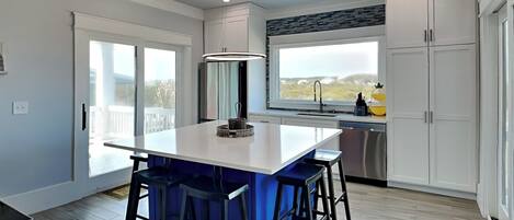 A modern kitchen with a central island, bar stools, a large window, and a view of the outdoors.