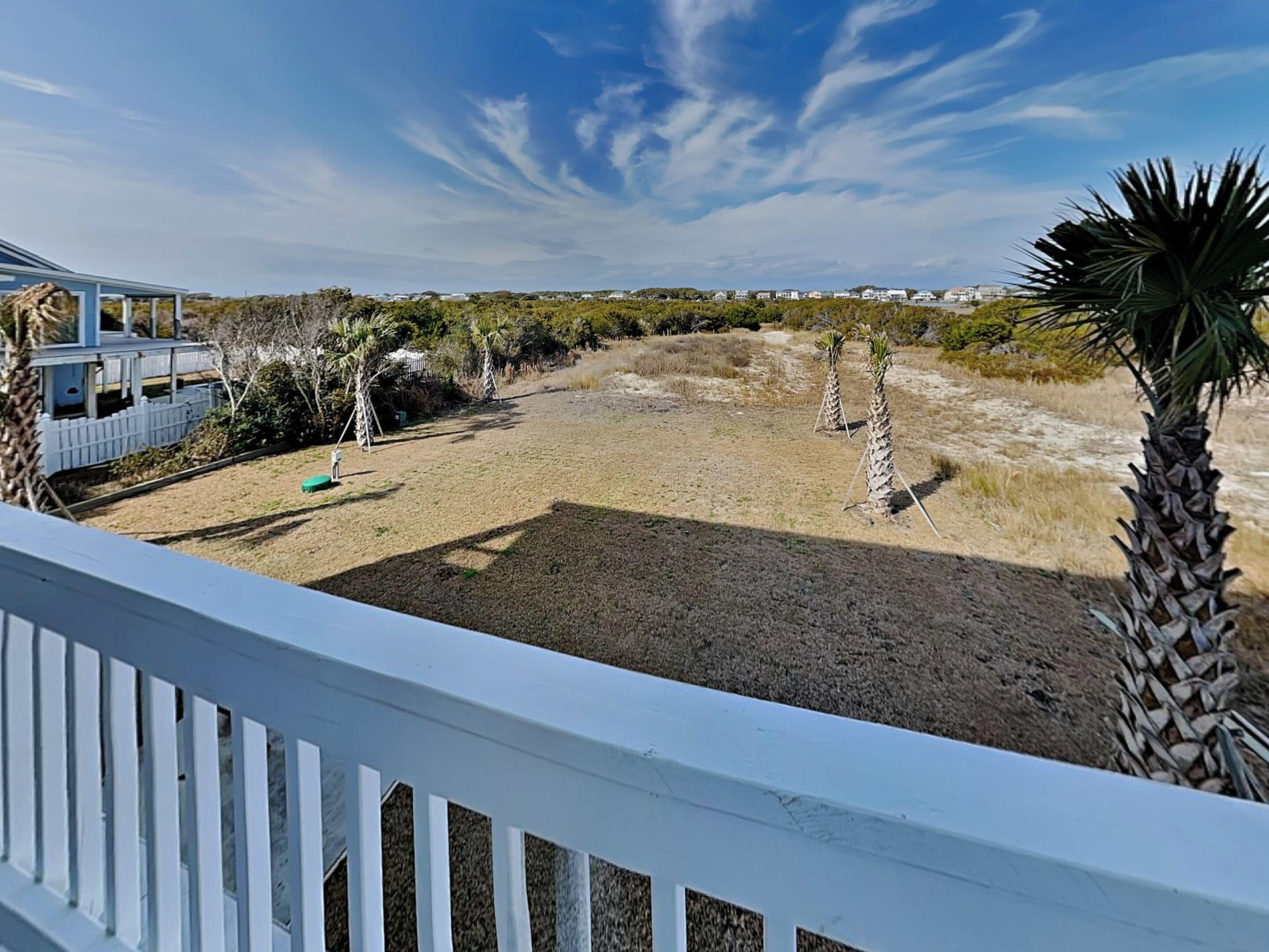 A view from a balcony overlooking a dry, open yard with sparse vegetation and a few palm trees.