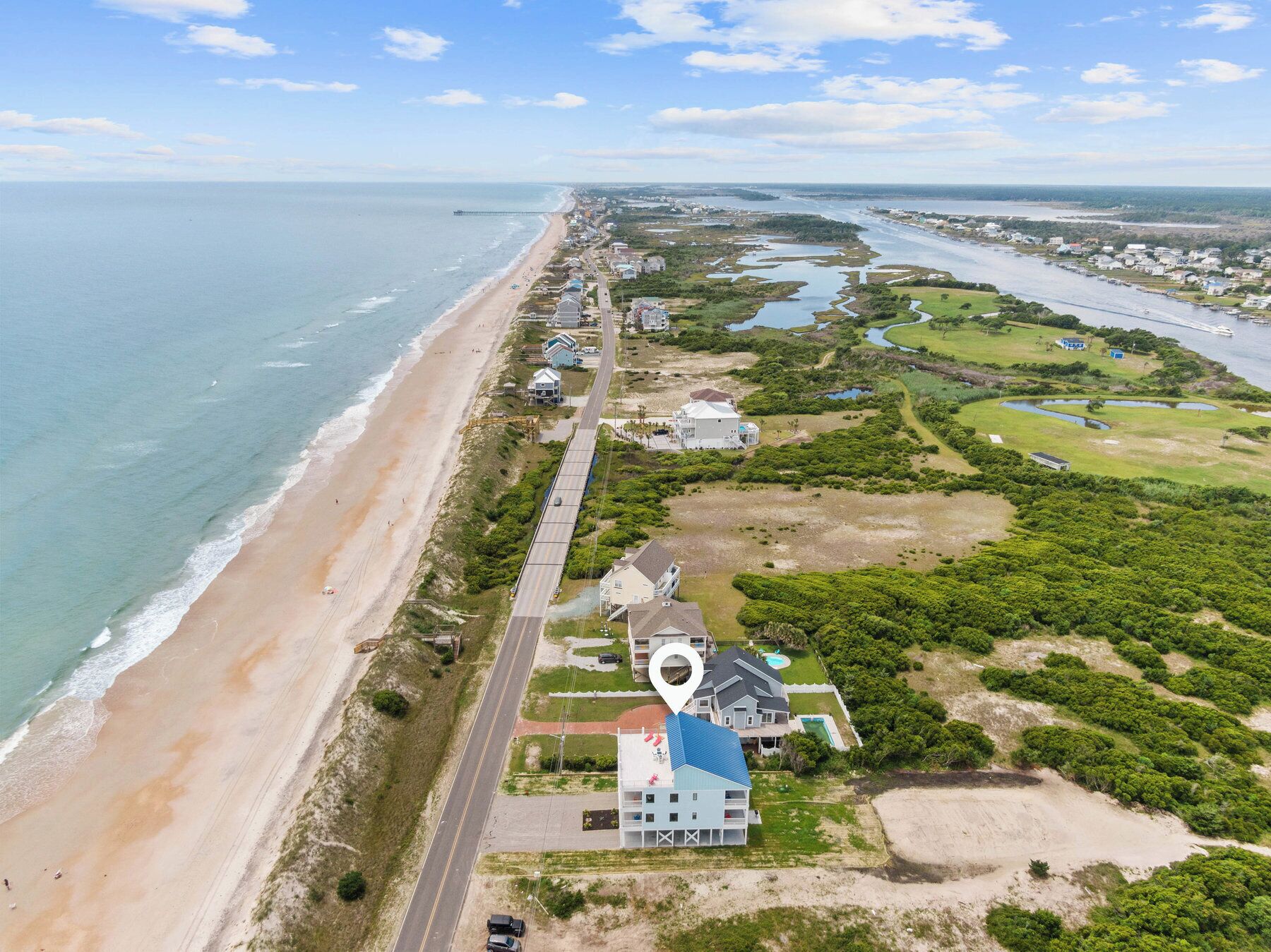 An aerial view of a coastal area with a beach, a road, and several buildings.