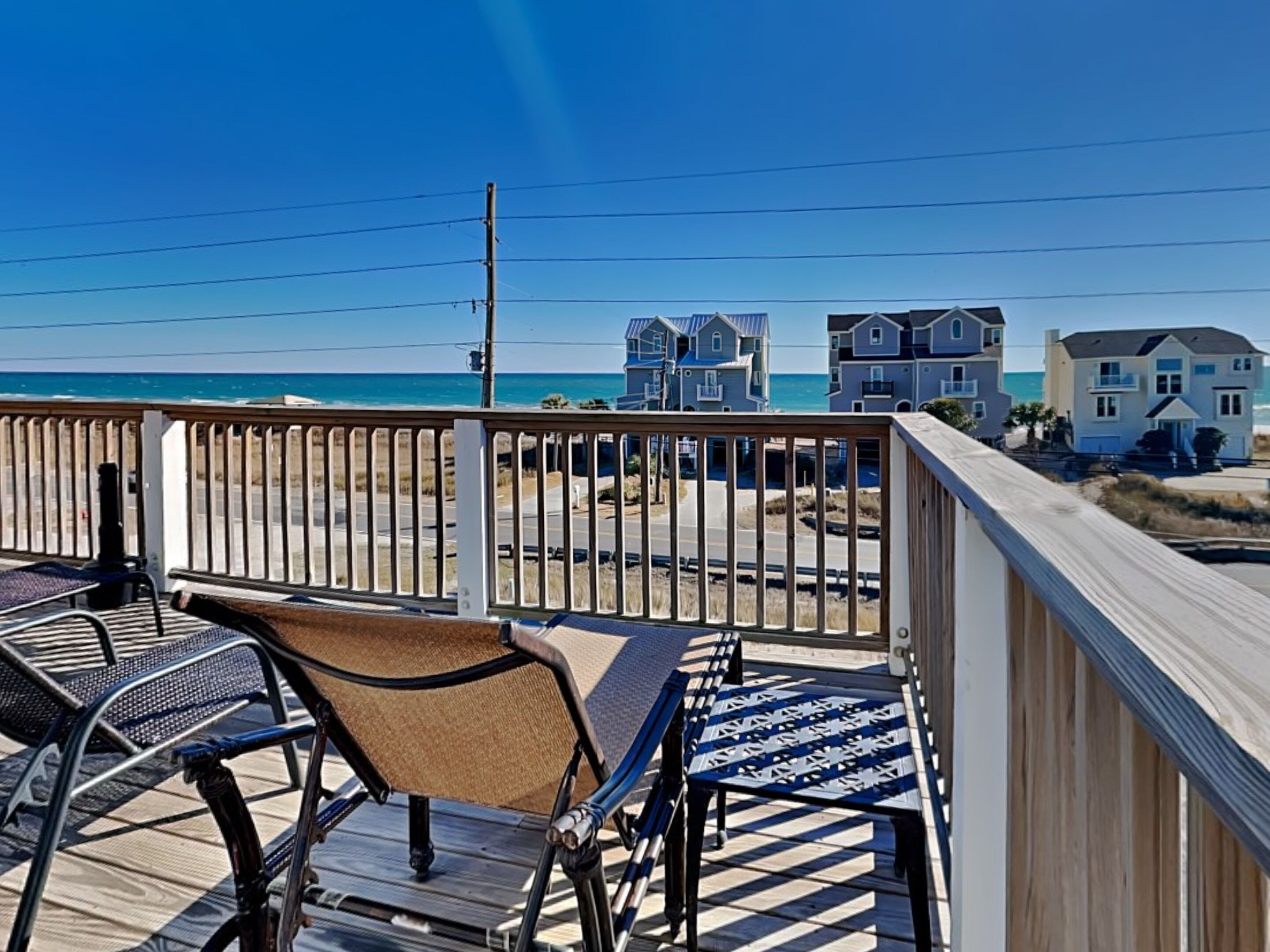 A deck with outdoor furniture overlooking a beach and houses.
