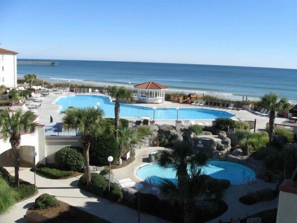 A resort with multiple swimming pools, palm trees, and a beach view.