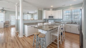 A spacious kitchen with a central island, white cabinetry, and a large window providing natural light. - Skipper's Hideout by Topsail Realty (Sneads Ferry)