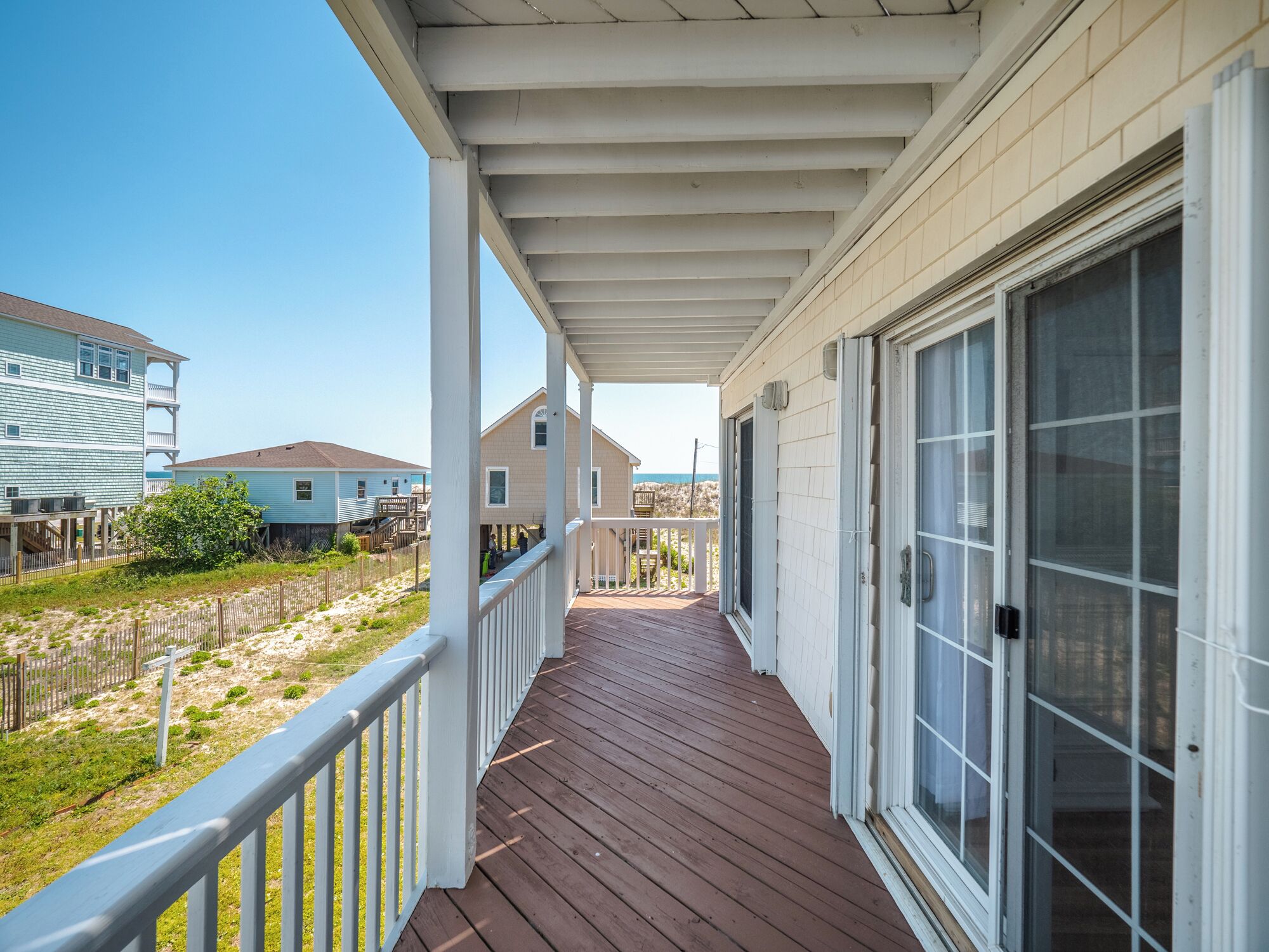 A covered porch with a wooden deck, white railings, and a large sliding glass door.