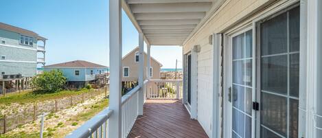 A covered porch with a wooden deck, white railings, and a large sliding glass door.
