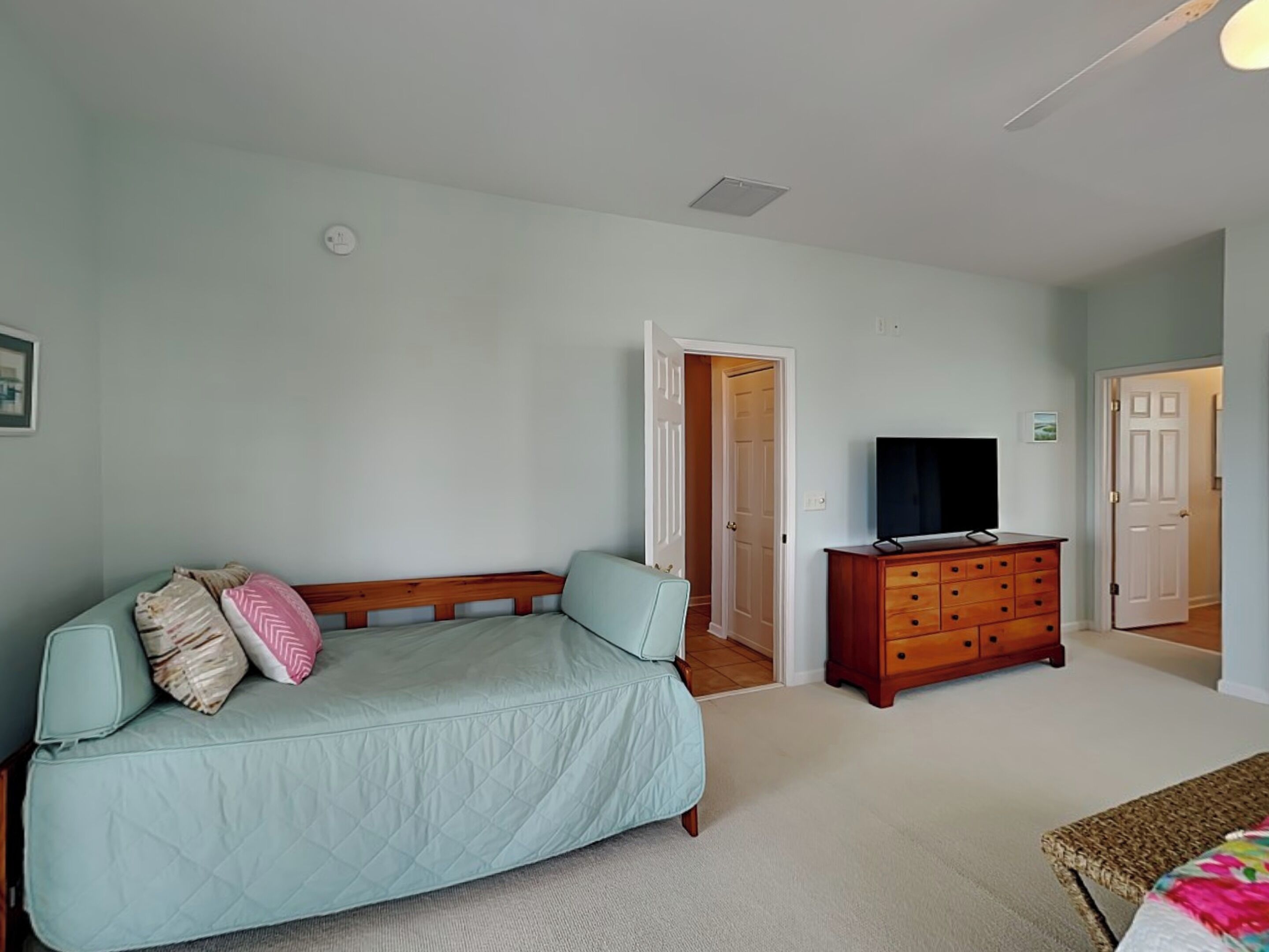 Quarto com um sofá azul claro, uma cômoda de madeira, uma televisão e uma porta que dá para outro espaço.