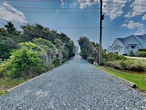 A gravel road flanked by greenery and residential houses. - Sunny Side Up by Topsail Realty (Sneads Ferry)