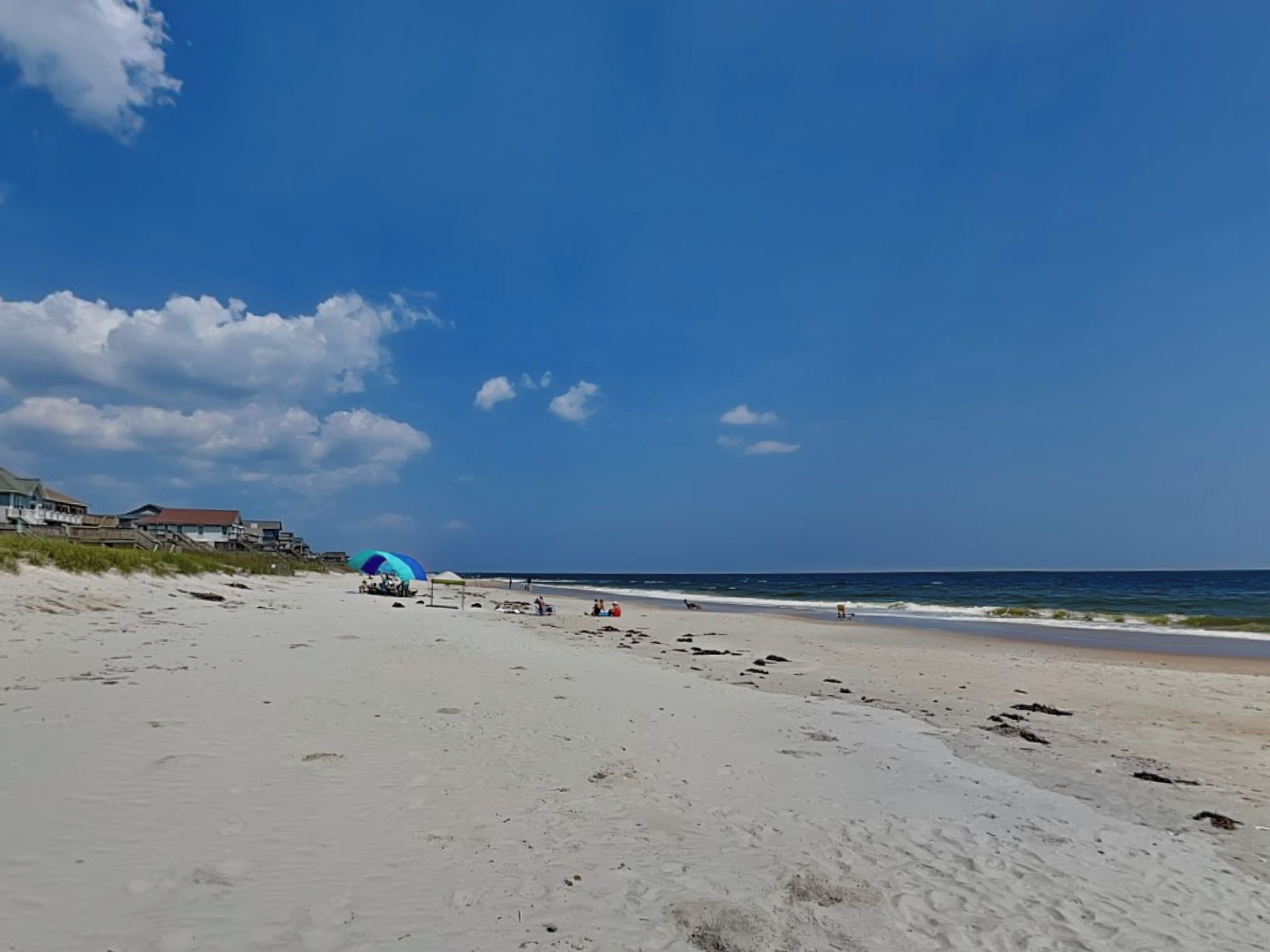 A wide sandy beach with footprints, a blue umbrella, and a few people.