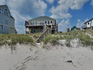 A beachfront house with a staircase leading to a balcony, surrounded by sand and vegetation. - Sunny Side Up by Topsail Realty (Sneads Ferry)