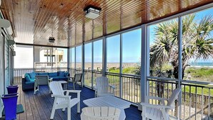 A covered outdoor deck with white Adirondack chairs, a blue sofa, and a small table. - Blue Me A Wave by Topsail Realty (Sneads Ferry)
