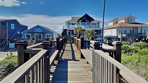 A wooden boardwalk leading to a beachfront property with multiple houses. - Blue Me A Wave by Topsail Realty (Sneads Ferry)
