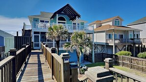 A wooden boardwalk leading to a multi-story house with a balcony and a covered porch. - Blue Me A Wave by Topsail Realty (Sneads Ferry)