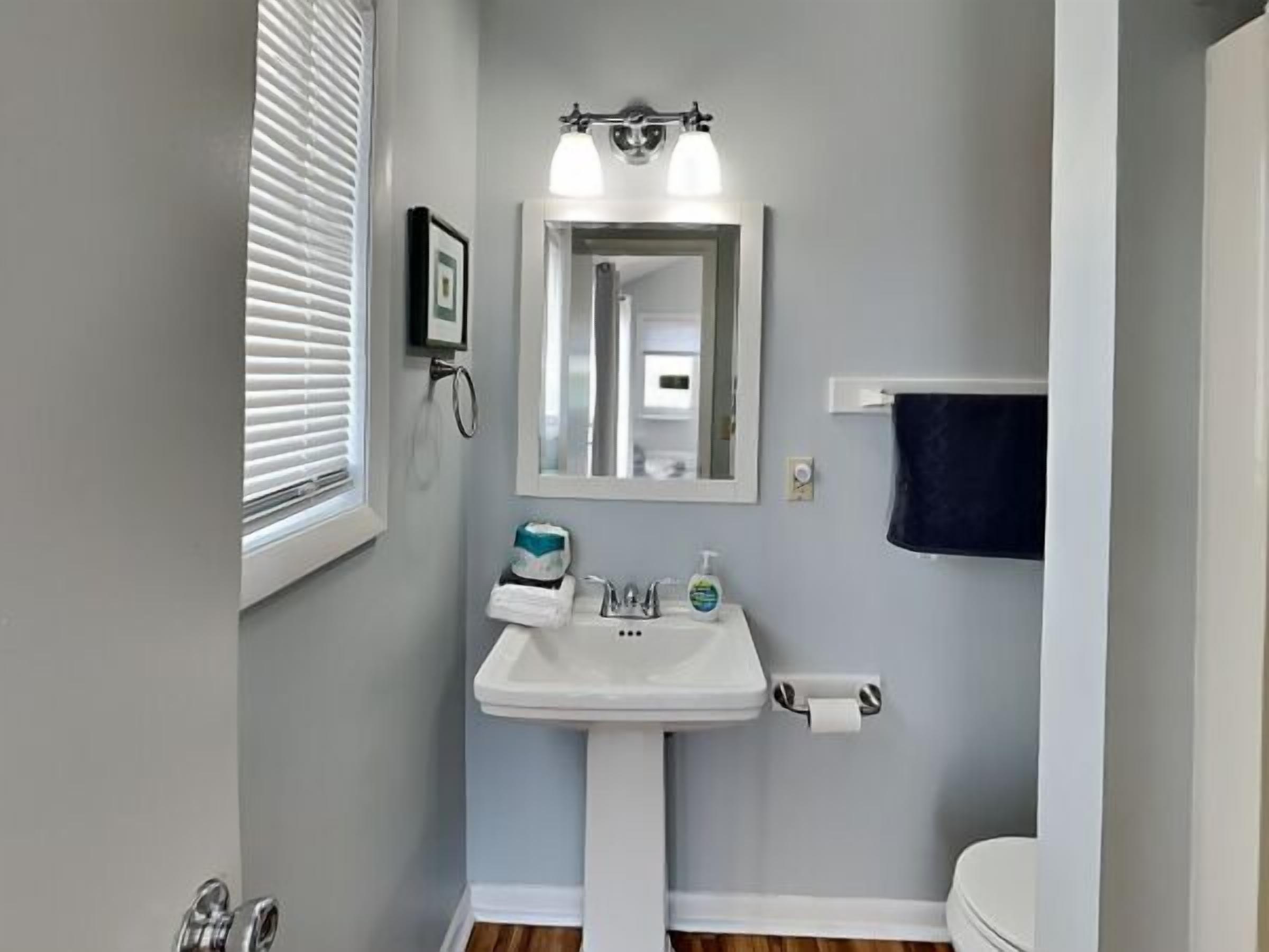 A bathroom with a white pedestal sink, a mirror above it, and a towel hanging on the wall.