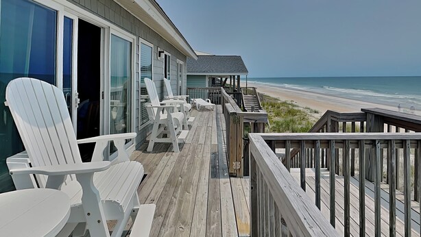 A wooden deck with white Adirondack chairs and a covered seating area overlooking a beach. - Hicks by Topsail Realty (Holly Ridge)