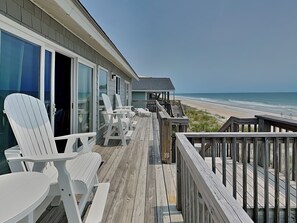 A wooden deck with white Adirondack chairs and a covered seating area overlooking a beach. - Hicks by Topsail Realty (Holly Ridge)