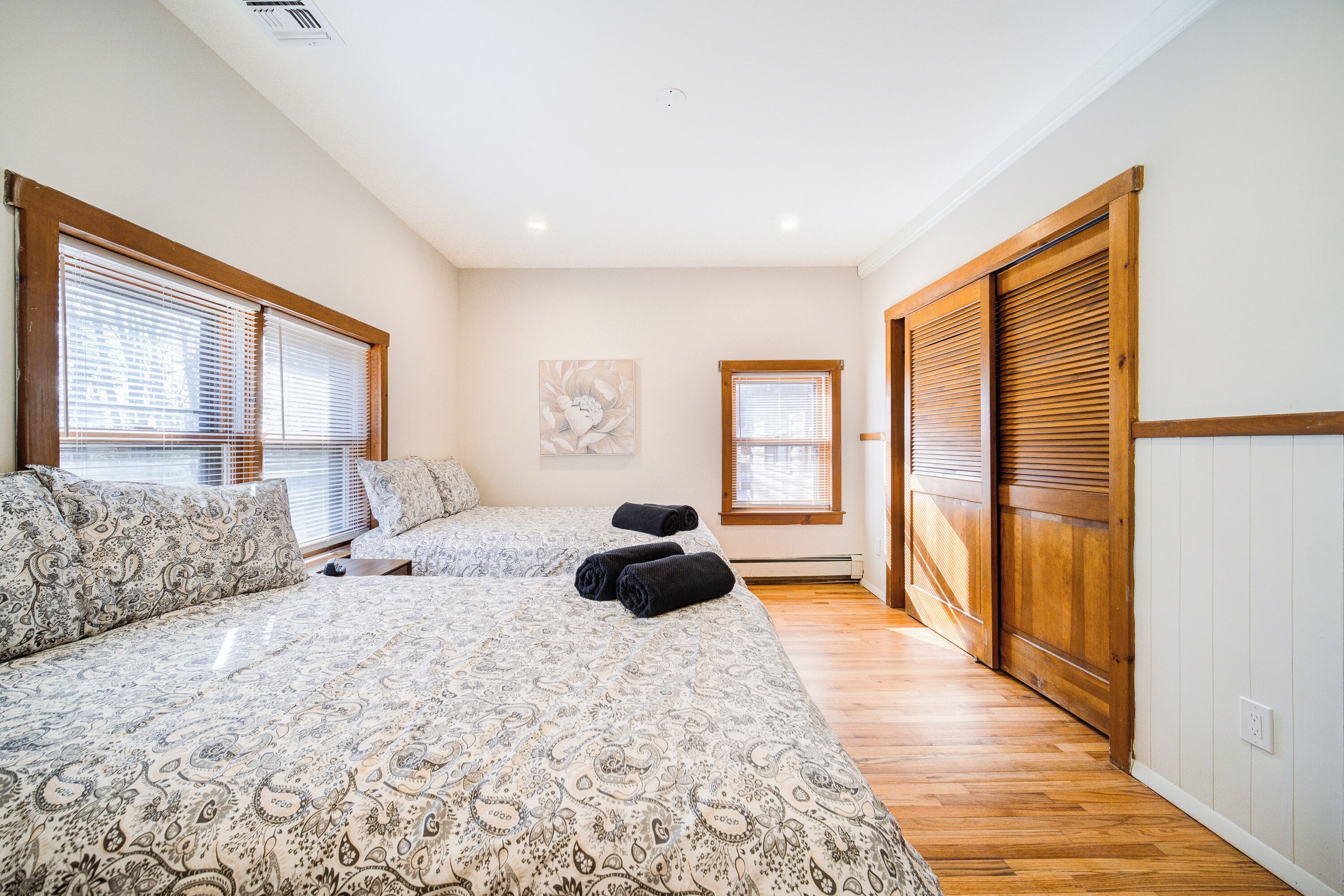 A bedroom with two beds, wooden flooring, and a sliding door closet.