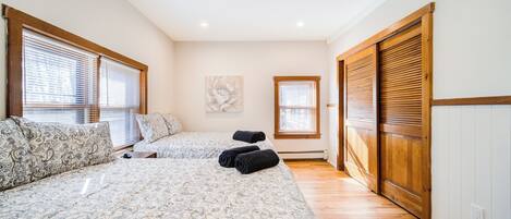 A bedroom with two beds, wooden flooring, and a sliding door closet.