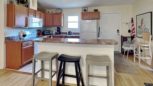 A modern kitchen with wooden cabinets, a granite countertop, and a central island with bar stools. - Sassy Seahorse by Topsail Realty (Holly Ridge)