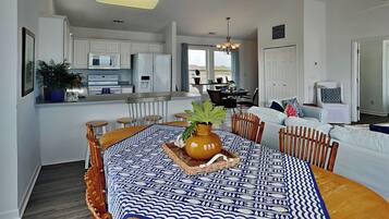 A modern kitchen with white cabinets, a dining area with a patterned tablecloth, and a living room with a sofa and chairs.