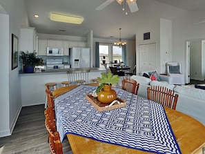 A modern kitchen with white cabinets, a dining area with a patterned tablecloth, and a living room with a sofa and chairs. - You're The Tops by Topsail Realty (Holly Ridge)