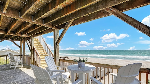 A wooden deck with white chairs and a table, overlooking a beach with a clear sky. - You're The Tops by Topsail Realty (Holly Ridge)