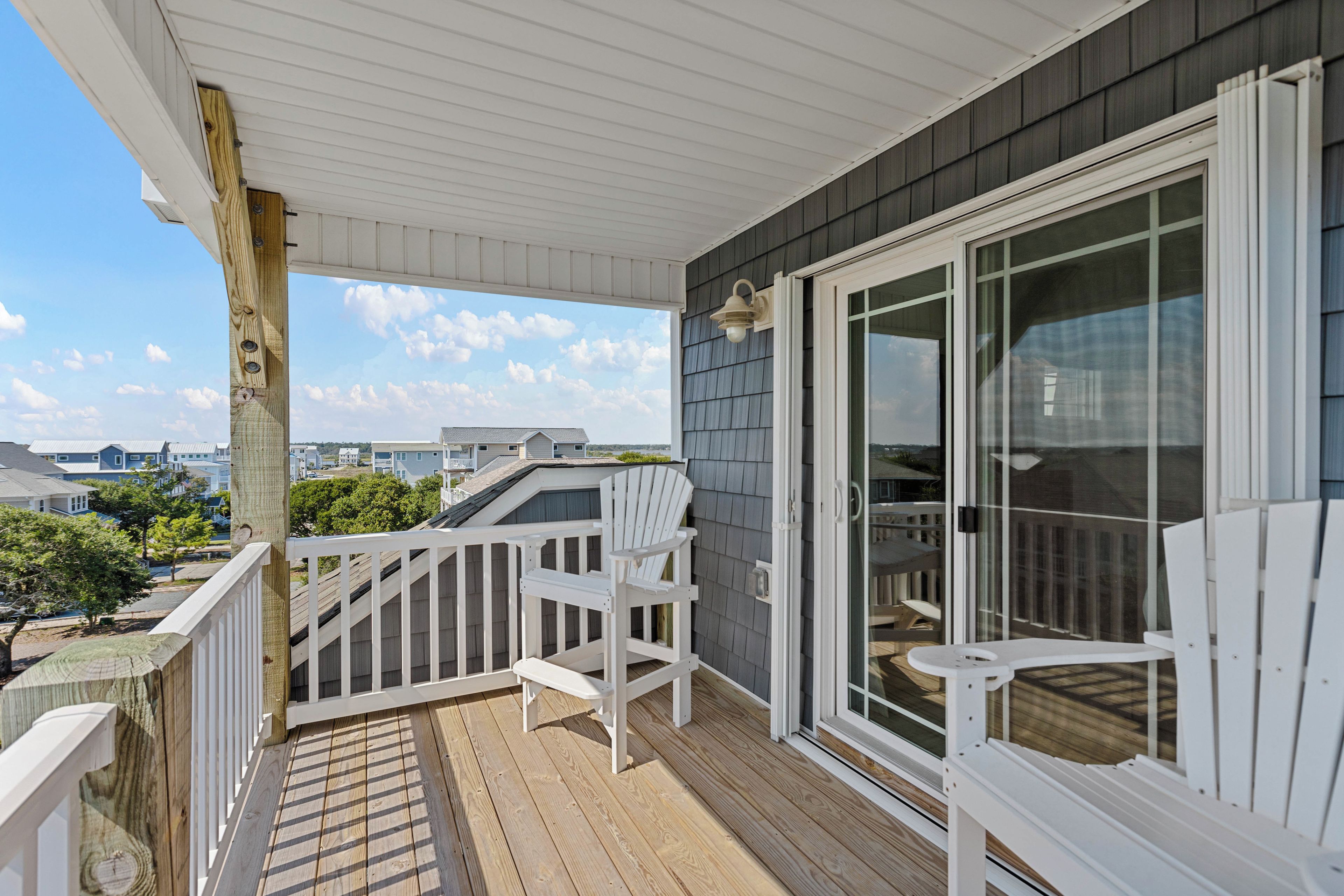 A wooden deck with white railings and chairs, a sliding glass door, and a view of neighboring houses.