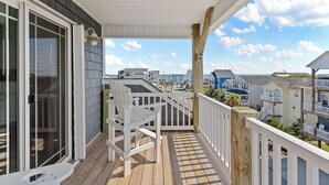 A wooden deck with a white railing, a white chair, and a glass door leading to a shaded area.
