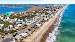 An aerial view of a coastal residential area with houses along the beach, a clear blue sky, and a calm sea.