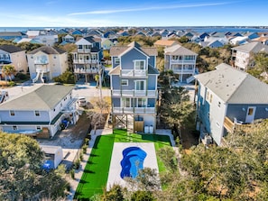 A coastal residential area with multi-story houses, a green lawn, and a large blue mural. - Across the Pond by Topsail Realty (Holly Ridge)