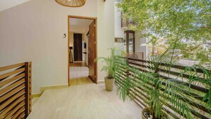 A hallway with a wooden floor, a wicker light fixture, a potted plant, and a staircase with a railing.