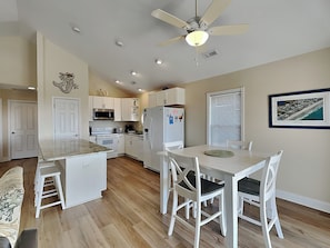 A modern kitchen with white cabinetry, a central island, and a dining area with white chairs. - Beach, Please by Topsail Realty (Holly Ridge)