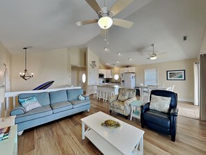 A living room with a sofa, armchair, coffee table, ceiling fans, and a kitchen in the background. - Beach, Please by Topsail Realty (Holly Ridge)