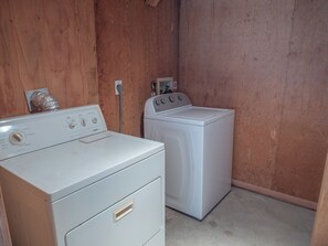 A laundry room with two white washers and dryers, wooden walls, and a visible electrical outlet. - Lungomare by Topsail Realty (Holly Ridge)
