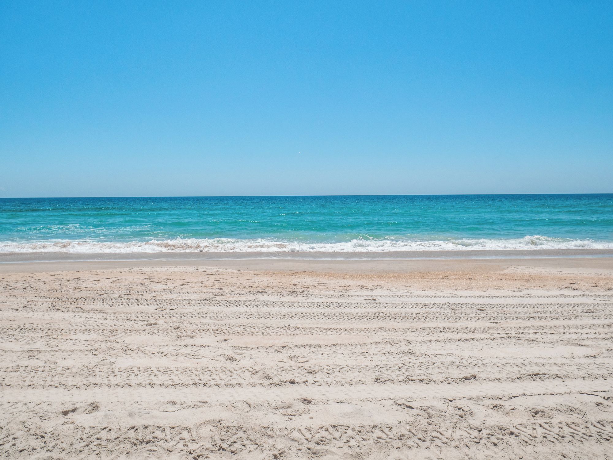 Une plage de sable fin, avec des vagues douces et un ciel bleu clair.
